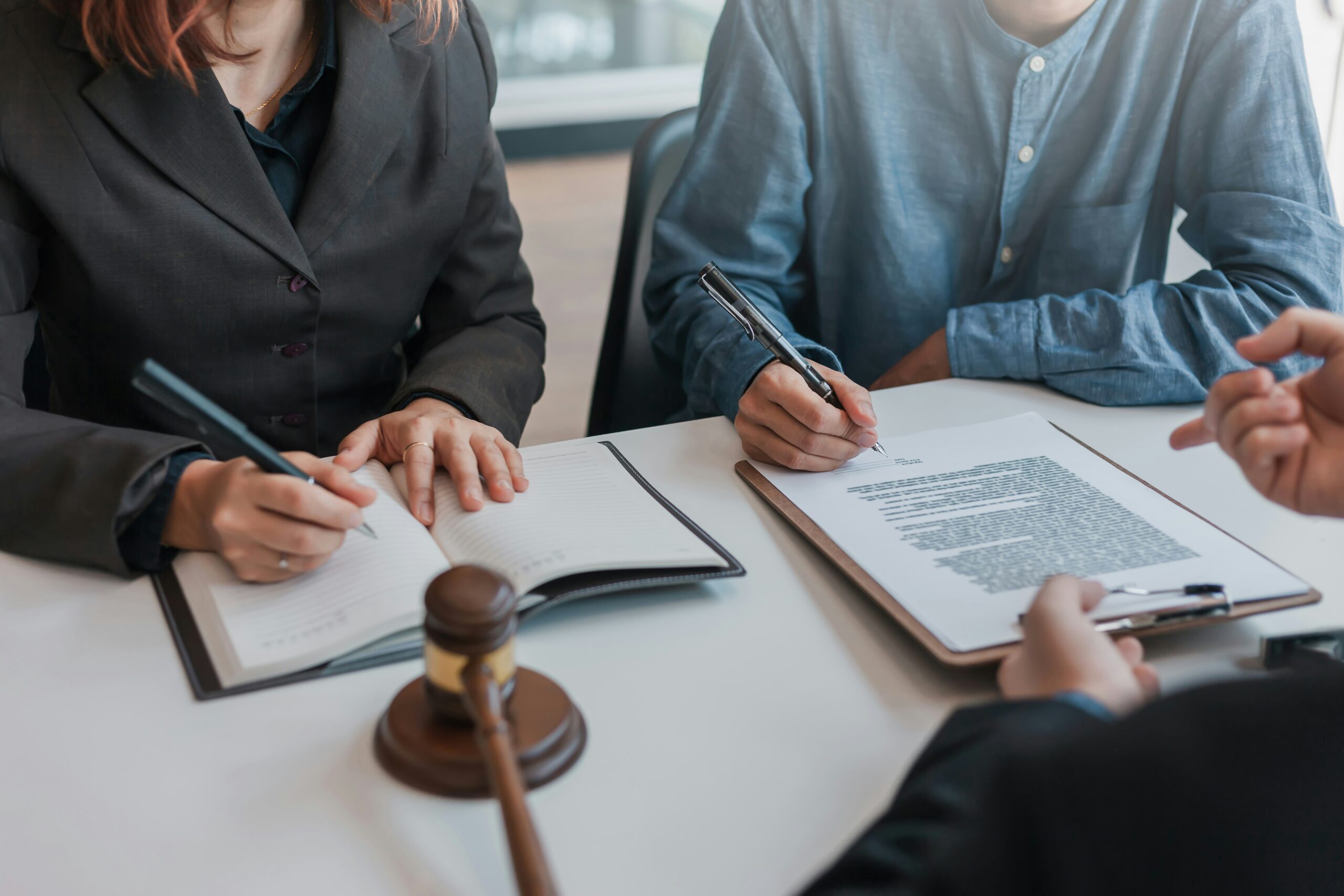 Two people seated at a table reviewing and signing legal documents, with a judge’s gavel in the foreground and a professional consultation taking place.