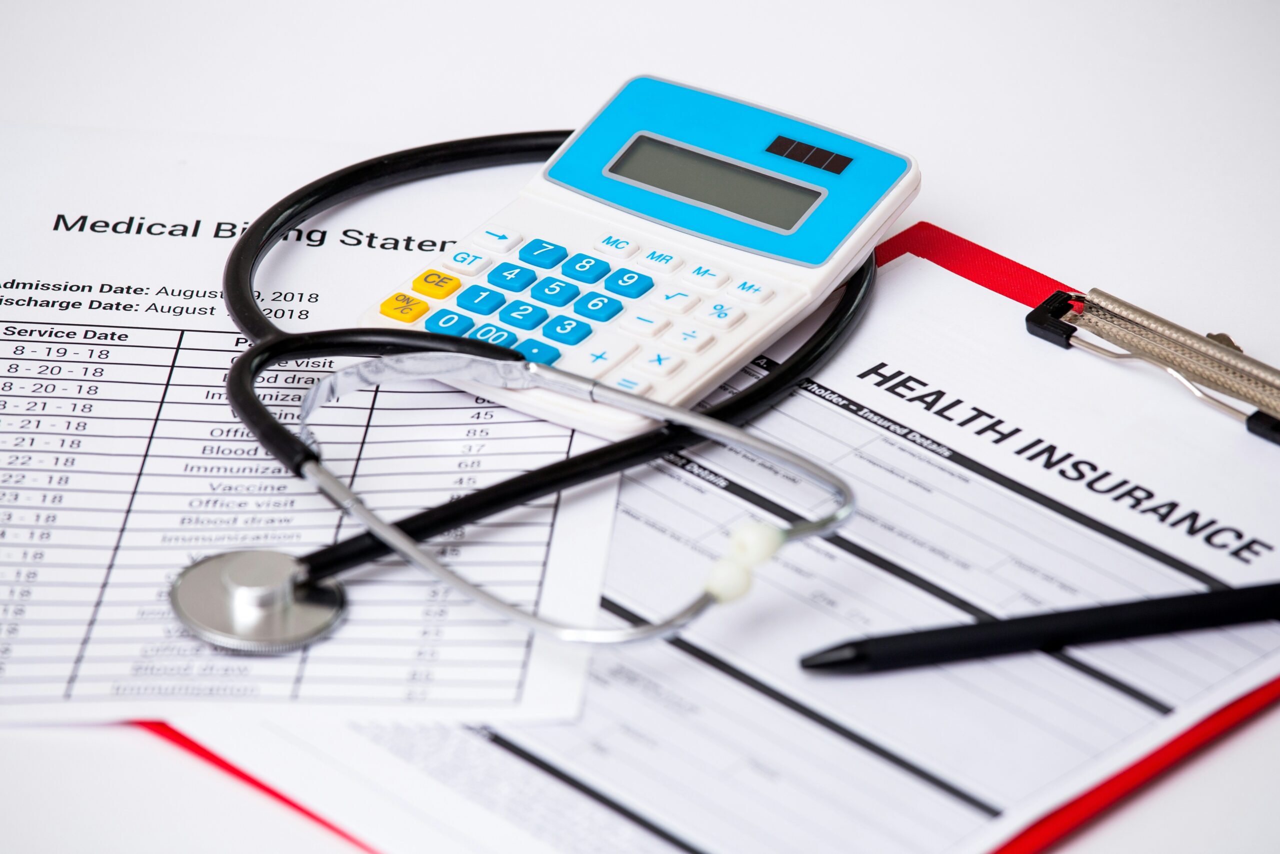 A stethoscope, calculator, and pen placed on top of medical billing statements and a health insurance form, suggesting calculations or review of healthcare costs.