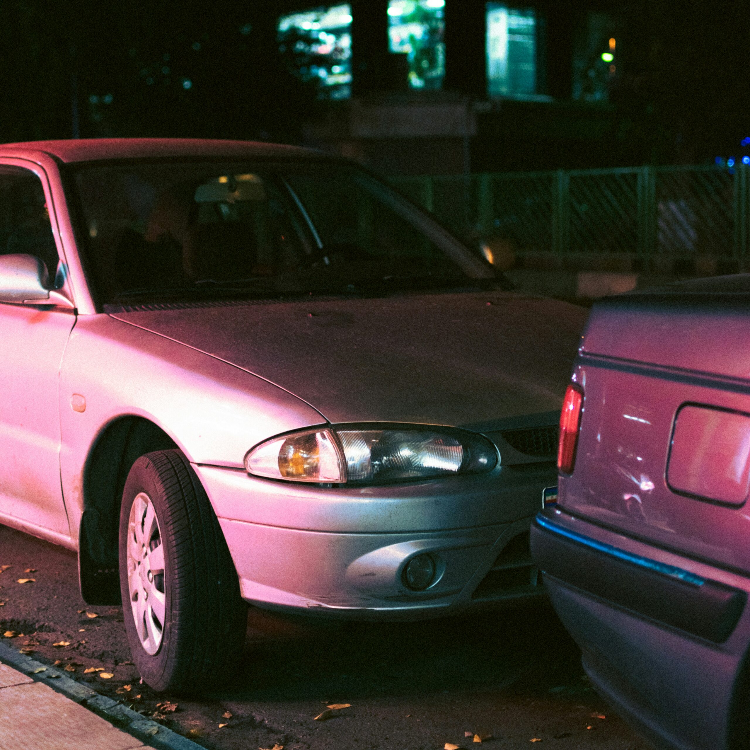 A pink car parked on the side of a road, surrounded by greenery and a clear blue sky.